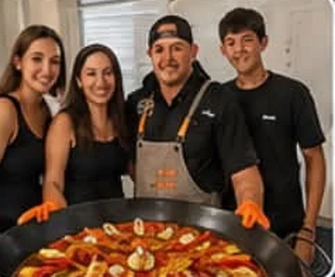 Invitados posando junto al chef detrás de la paellera terminada